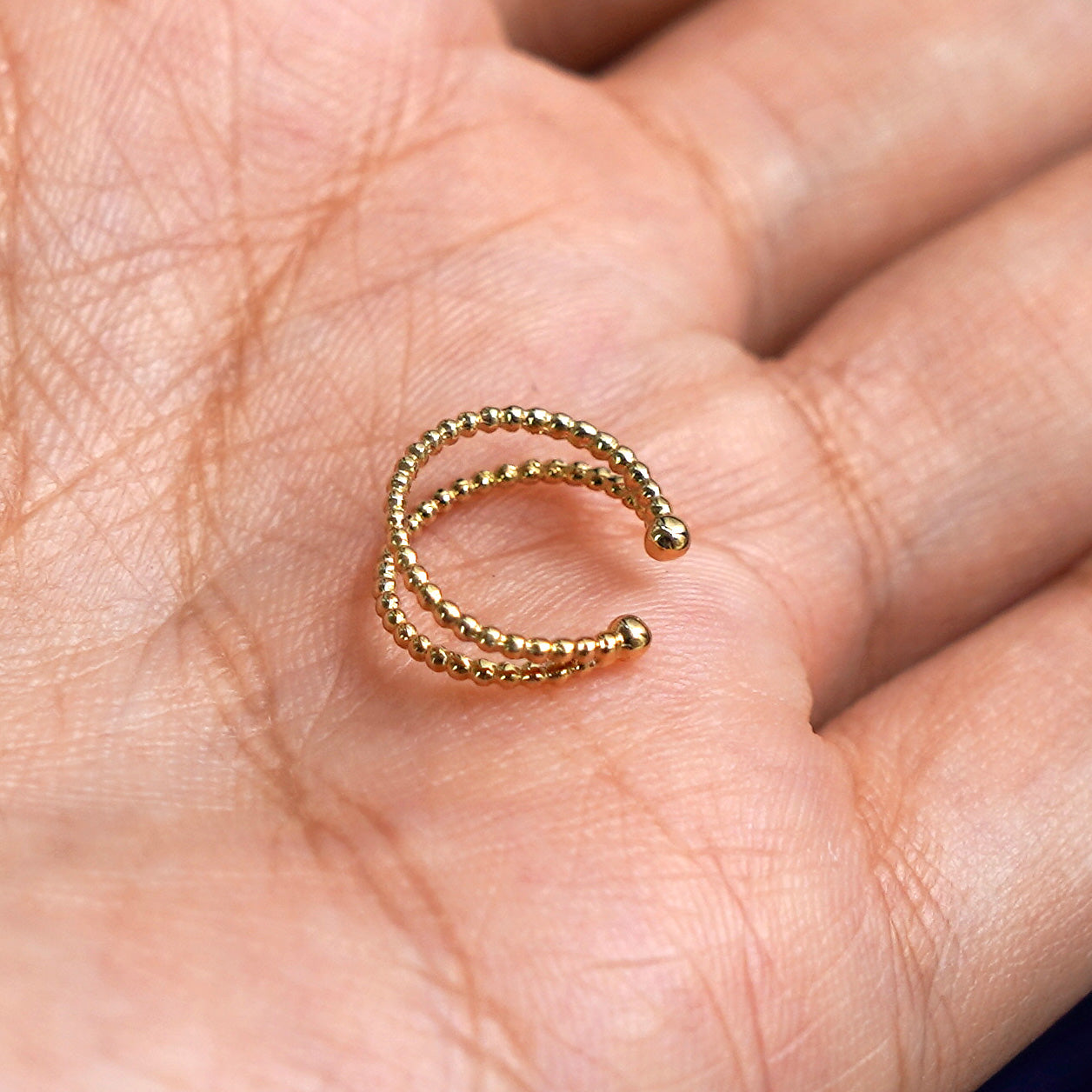 A solid yellow gold Beaded Cuff earring resting in a model's palm