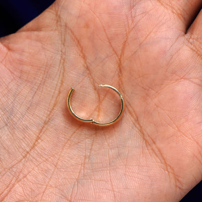 A solid 14k yellow gold Medium Thick Huggie Hoop Earring open in a model's palm to show the hinge