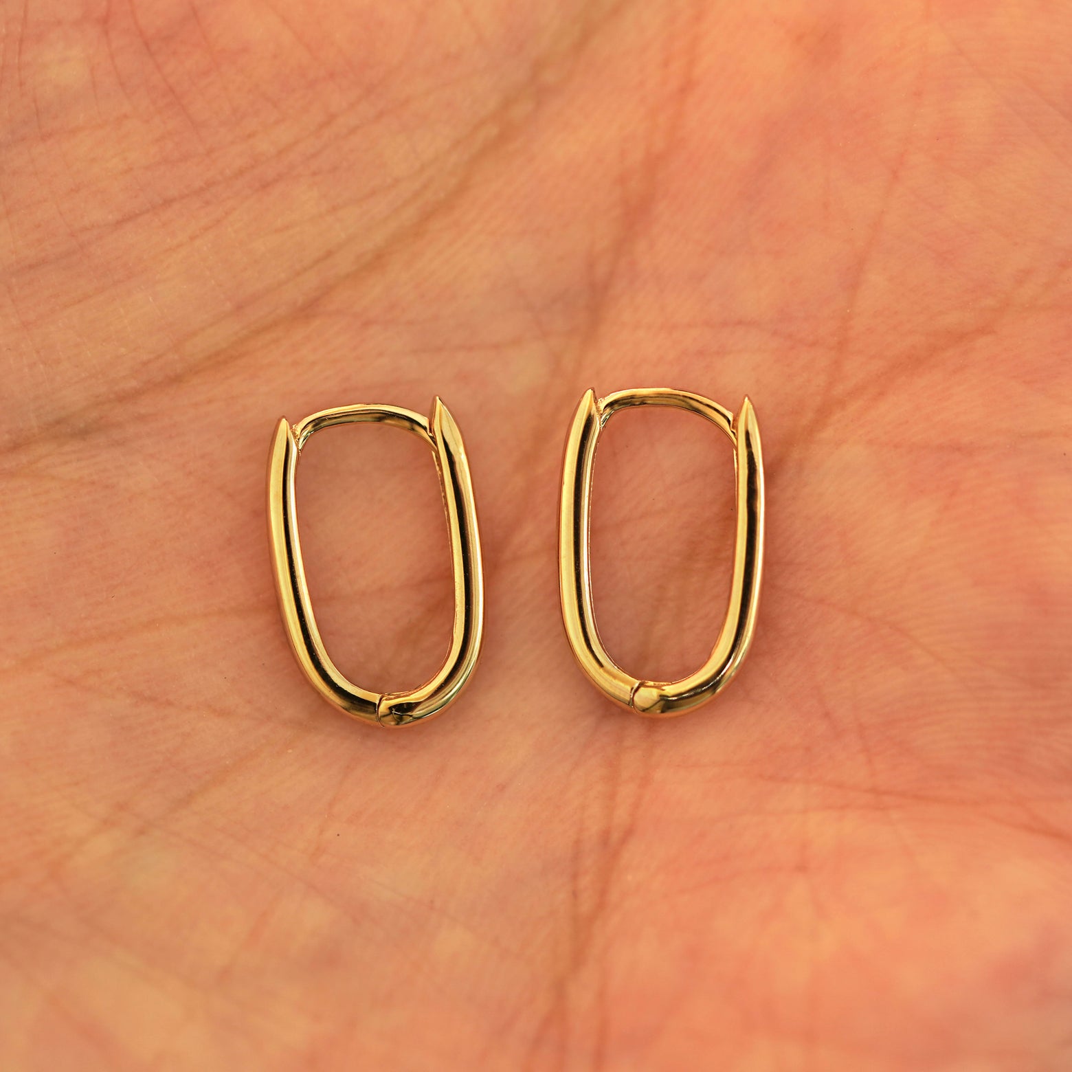 A pair of 14k yellow gold Thin Oval Huggie Hoops resting in a model's palm