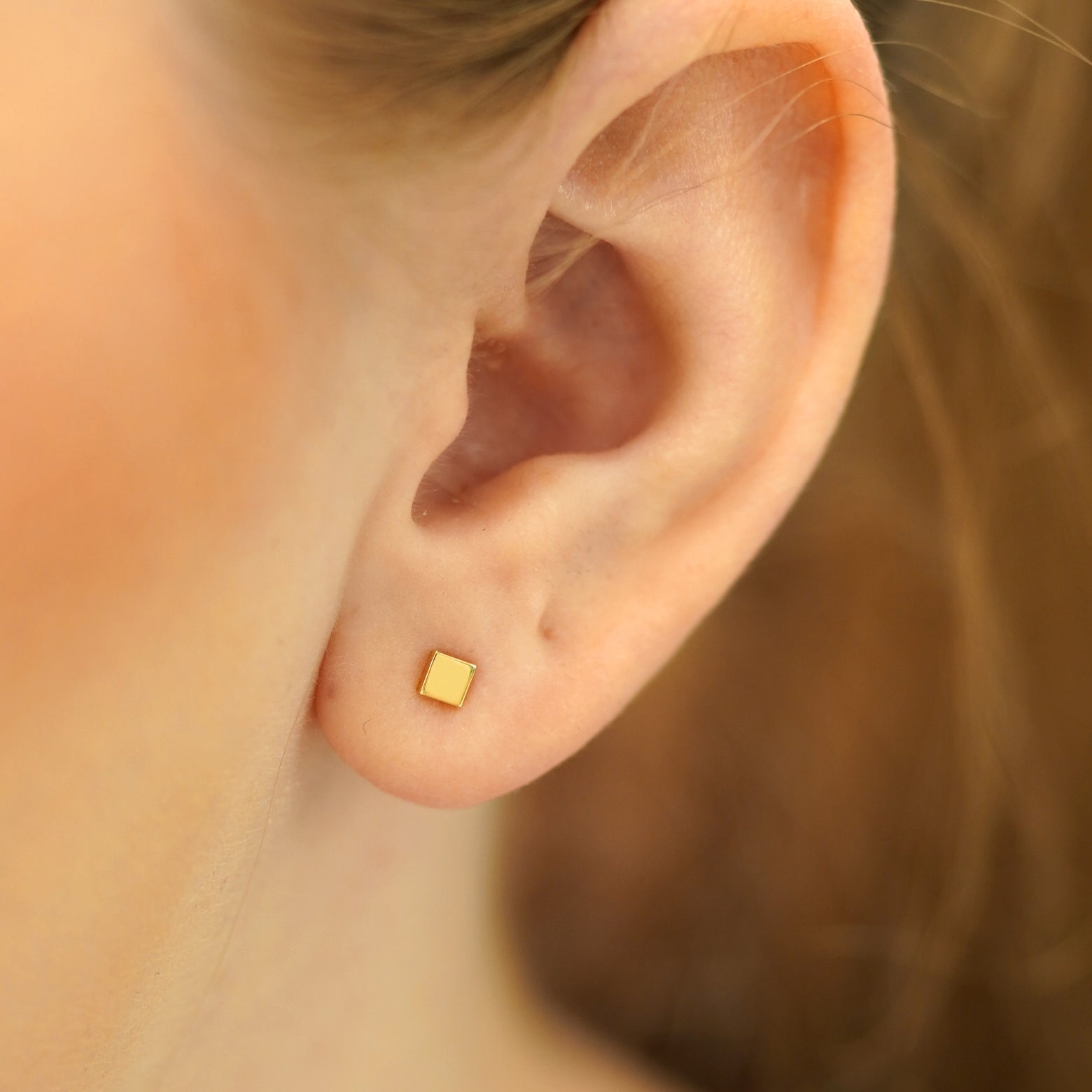 A model's ear wearing a solid yellow gold Square Earring