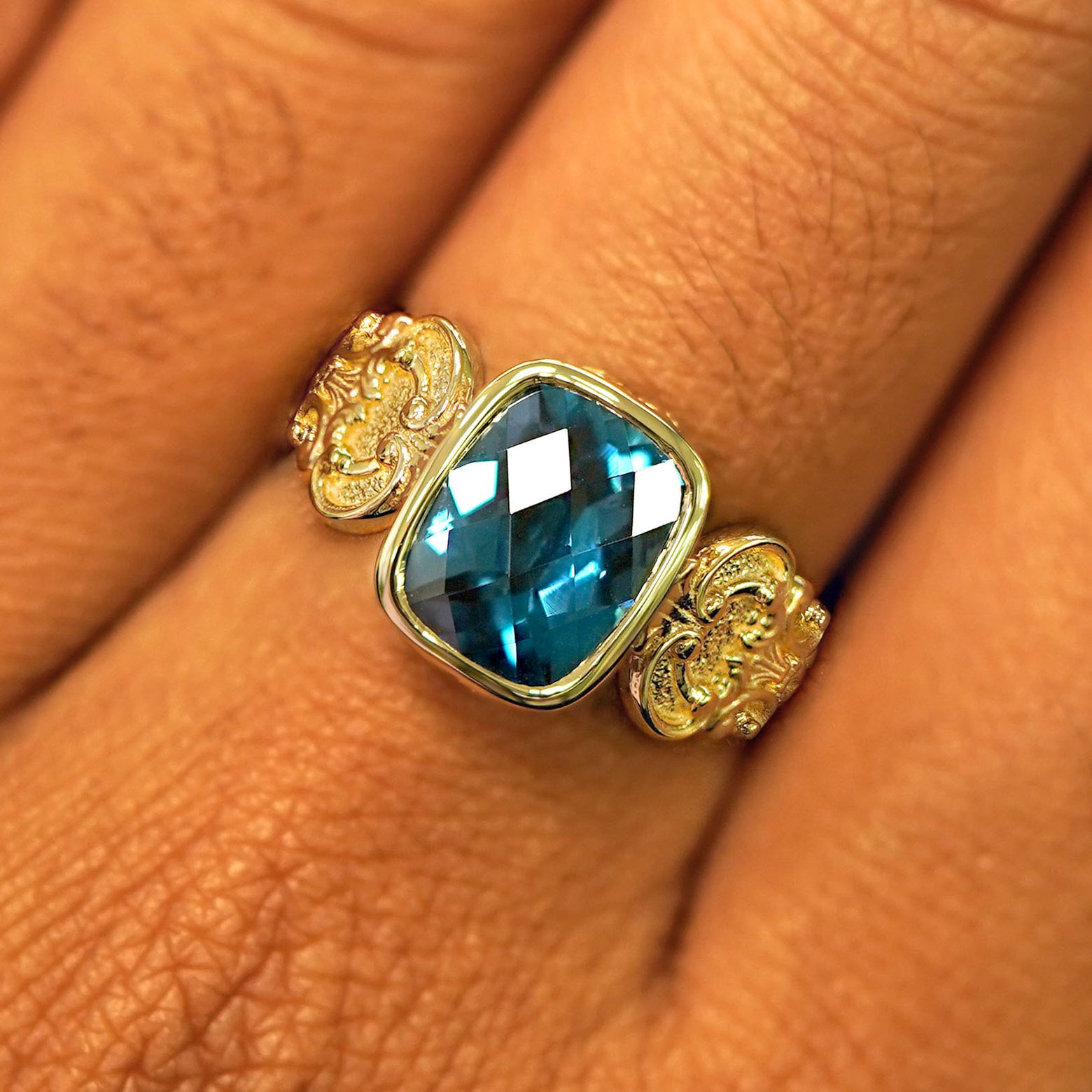 Close up view of a model's fingers wearing a yellow gold London blue topaz Royalty Ring