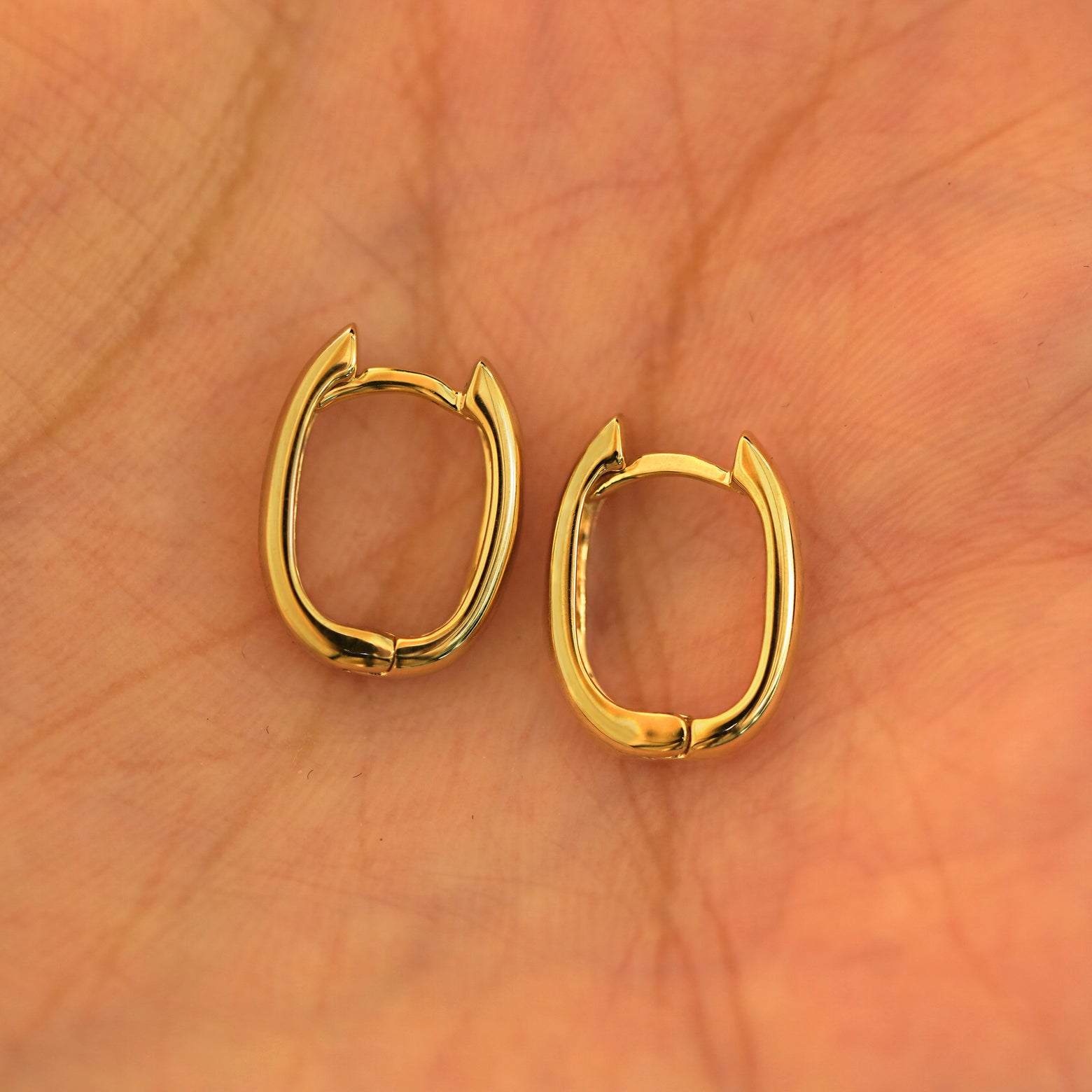 A pair of 14k yellow gold Thick Oval Huggie Hoops resting in a model's palm
