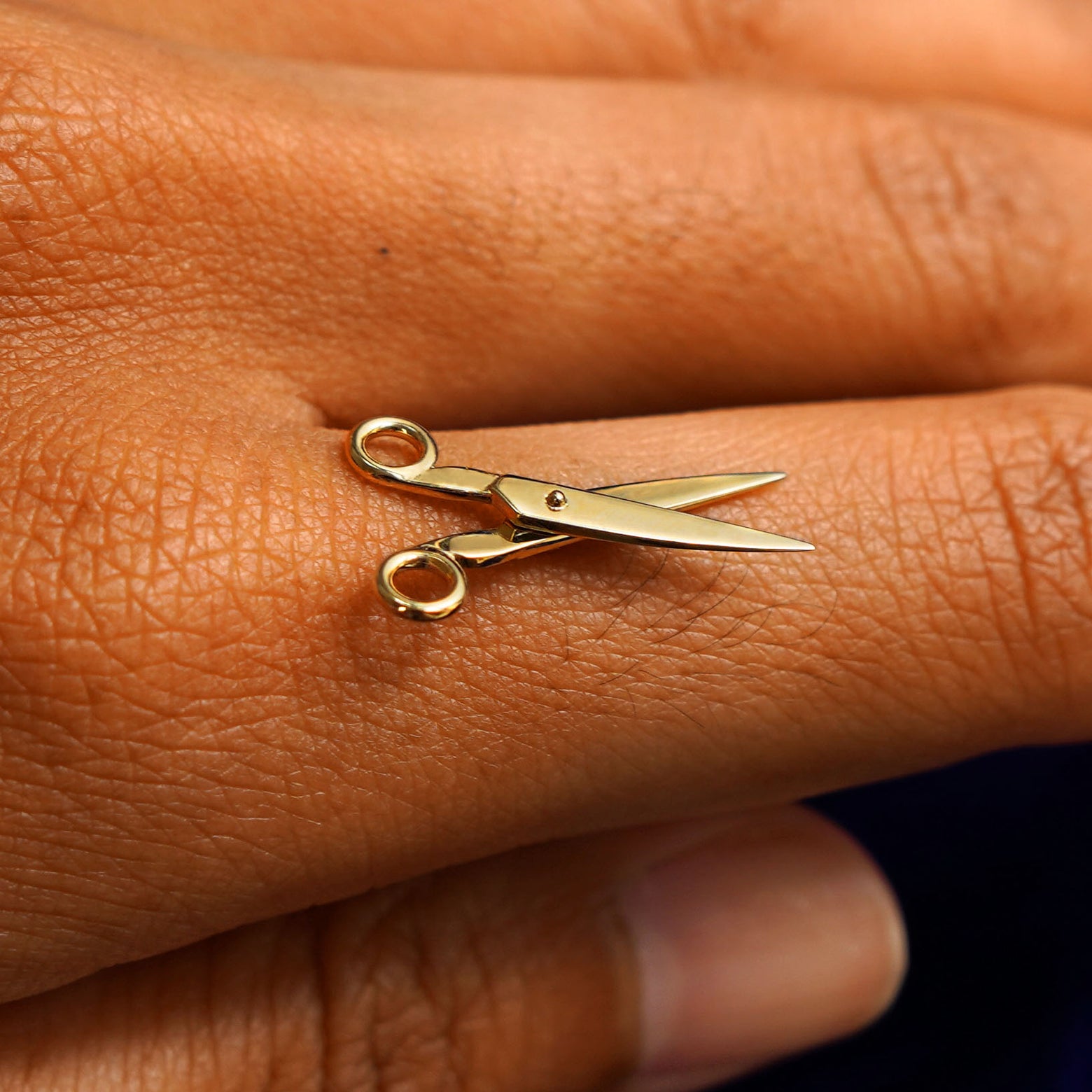 A 14k yellow gold Scissors Charm for earring balancing on the back of a model's finger