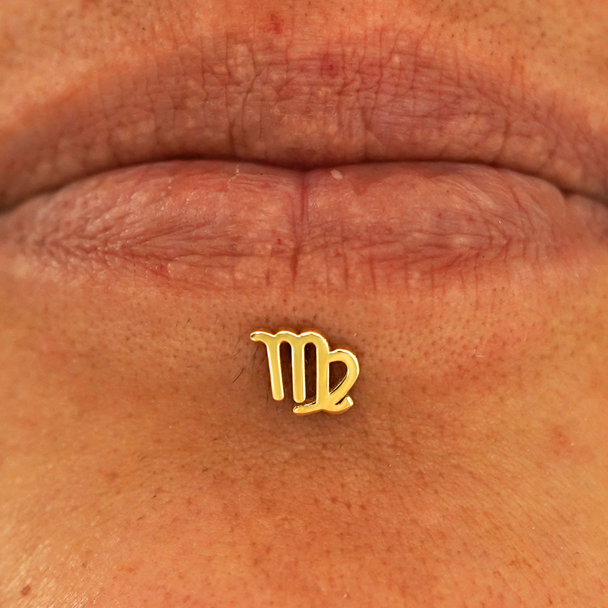 Close up view of a model's lips wearing a 14k yellow gold Virgo Horoscope Flatback in a labret piercing