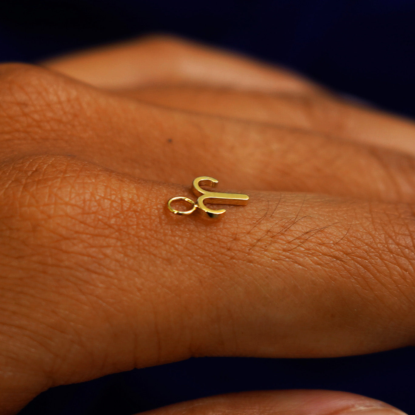 A solid yellow gold Aries Horoscope Charm for earring sitting on the back of a model's finger