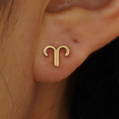Close up view of a model's ear wearing a 14k solid yellow gold Horoscope Earring with an Aries zodiac symbol