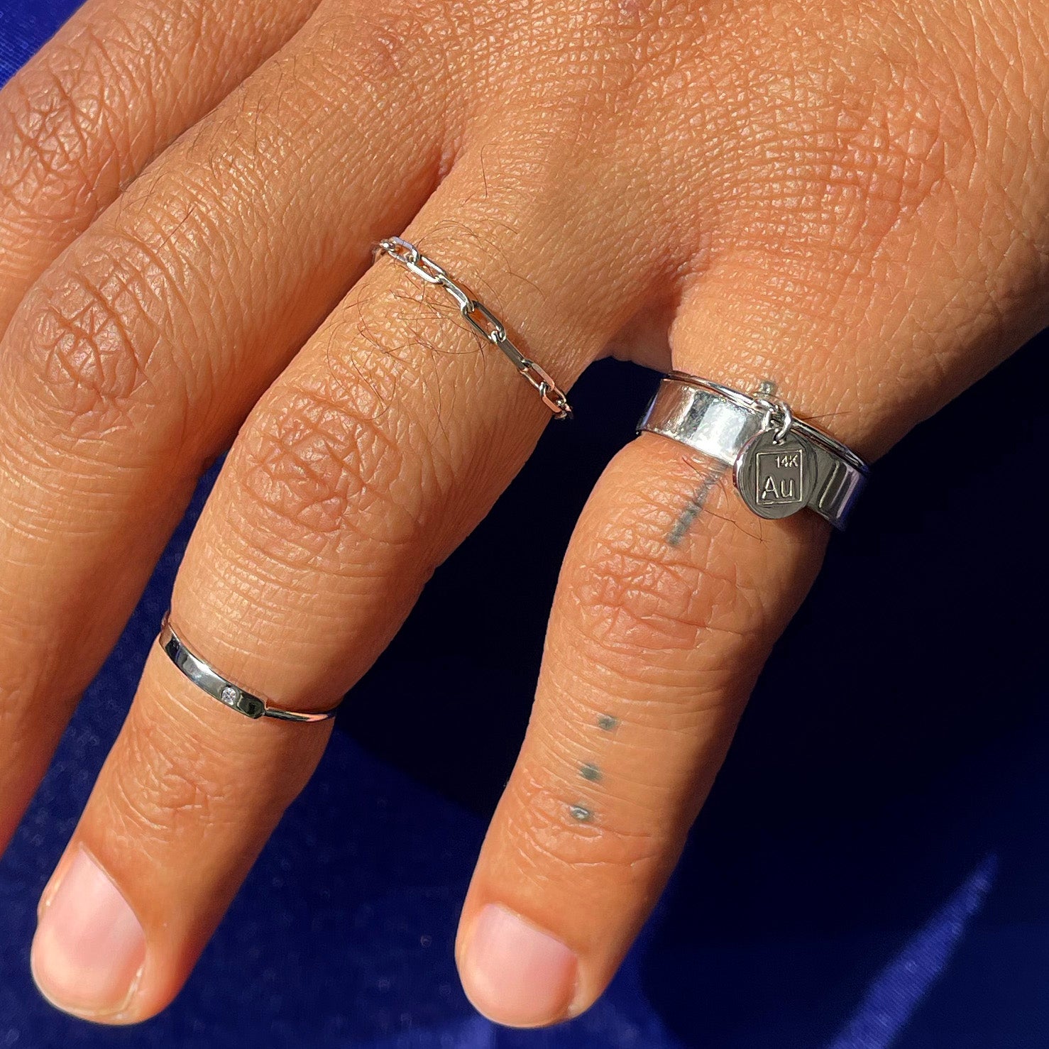 A model's ring and pinky fingers wearing a white gold Industrial Mirror Band, a Disk Ring,  Diamond Bar Ring, and Butch Ring