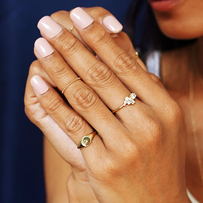 A model with their hands clasped in front of their face wearing a Diamond Cluster Ring, a Signet Ring, and a Bead Chain Ring