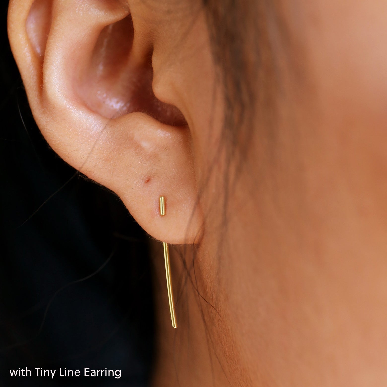 Close up view of a model's ear wearing a yellow gold Line Jacket with a Tiny Line Earring