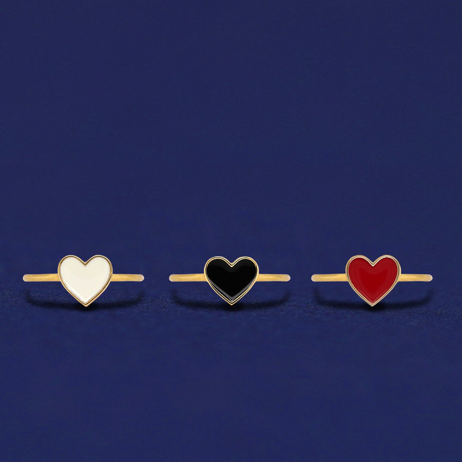 Three 14k yellow gold enamel heart rings shown in options of white, black, and red enamel