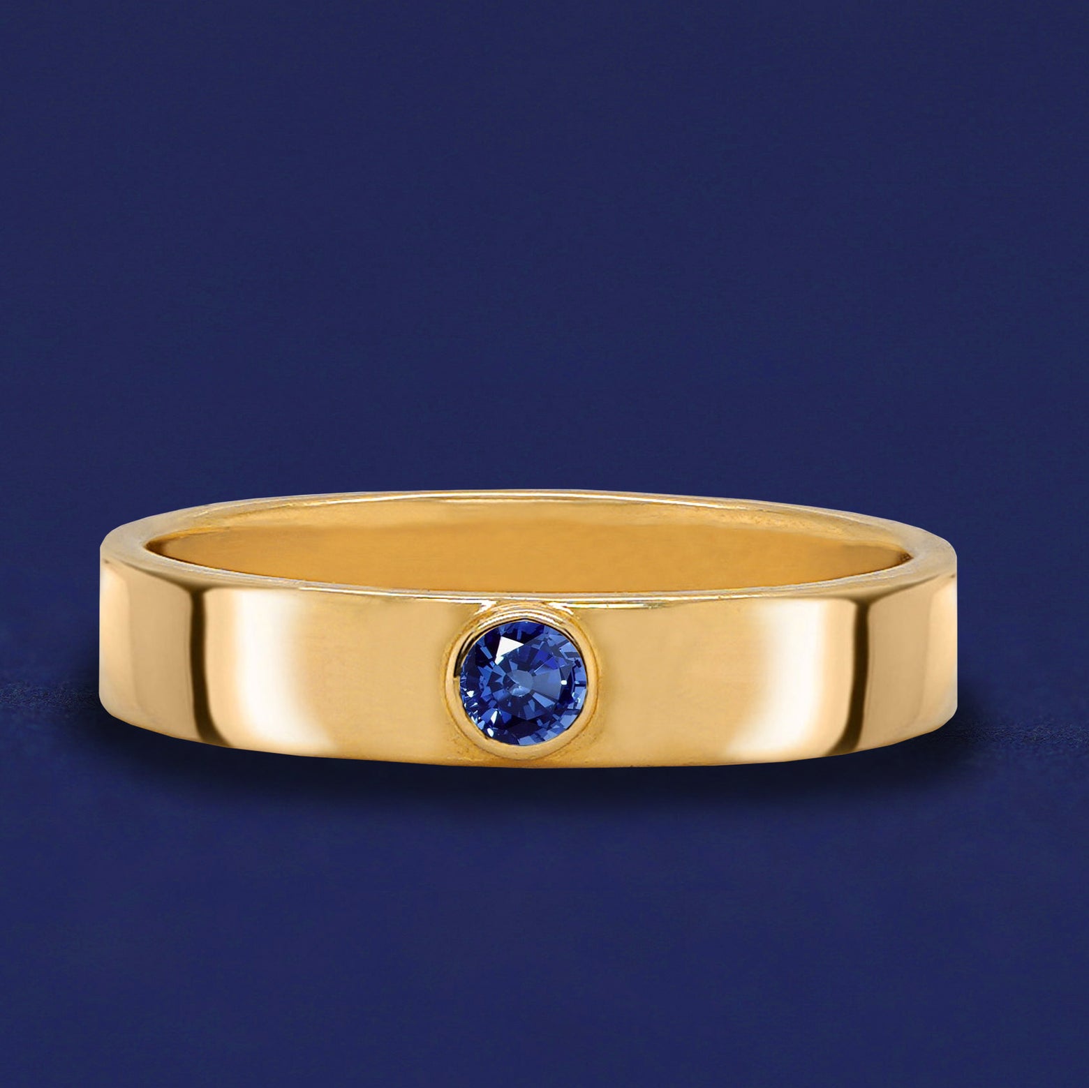 A 14 karat solid gold band ring with a bezel set sapphire gemstone