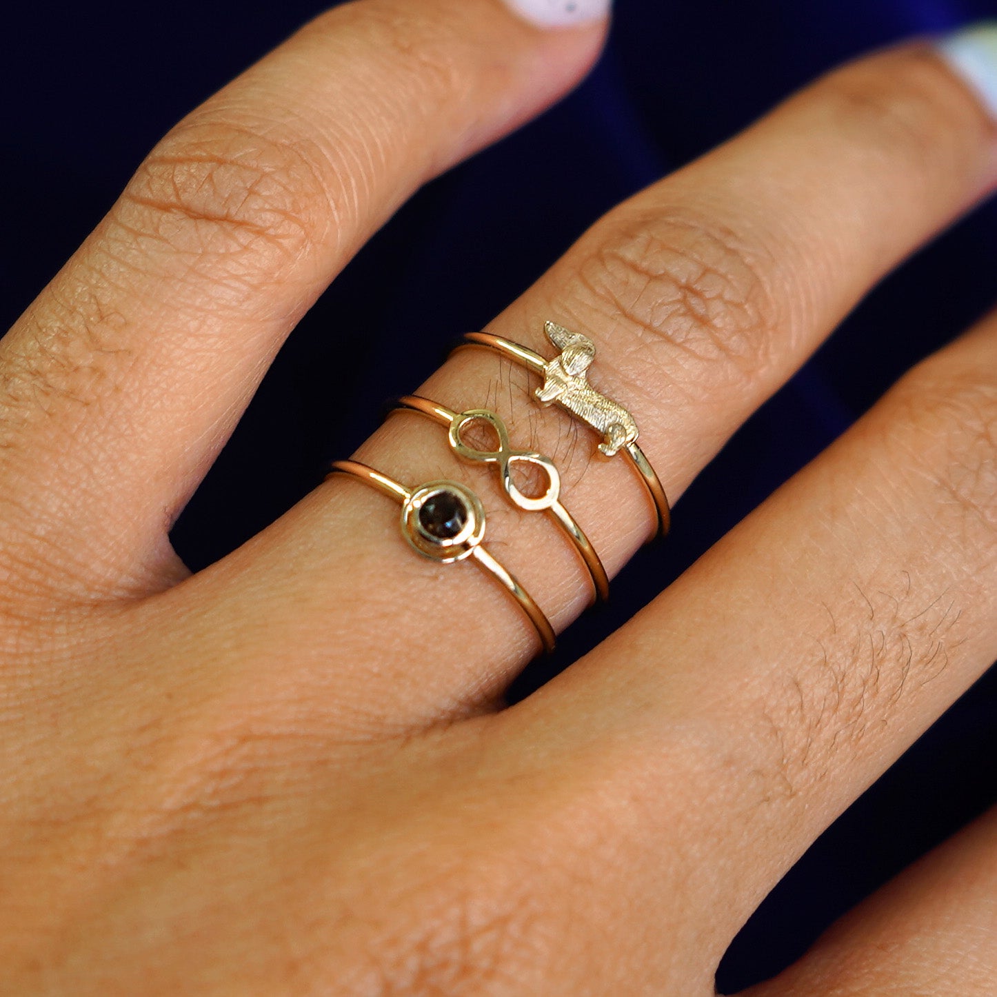 Close up view of a model's hand with an Infinity Ring, Dog Ring, and Coffee Cup Ring stacked on their finger