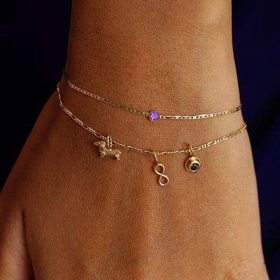 A model's wrist with Infinity, Dog, and Coffee Cup Charms on a Figaro Bracelet stacked with an Amethyst Bracelet