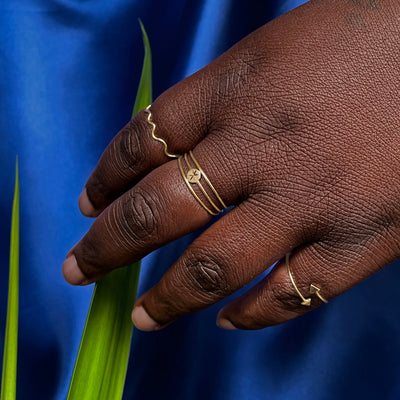 A model touching a plant leaf wearing a Star Disk Ring between two Line Rings and other Automic Gold rings