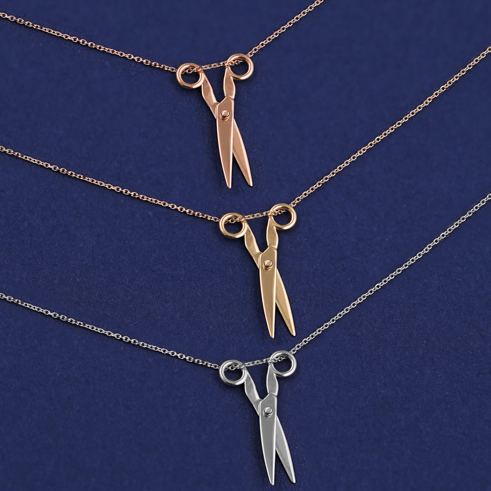 Three versions of the Scissors Necklace shown in options of rose, yellow, and white gold