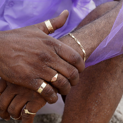 A model on the beach clasping their wrist with a sandy hand while wearing Automic Gold jewelry
