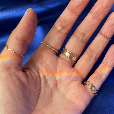 A hand wearing various yellow gold Automic Gold rings with a rainbow cast across their palm
