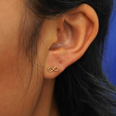 Close up view of a model's ear wearing a yellow gold Infinity Earring