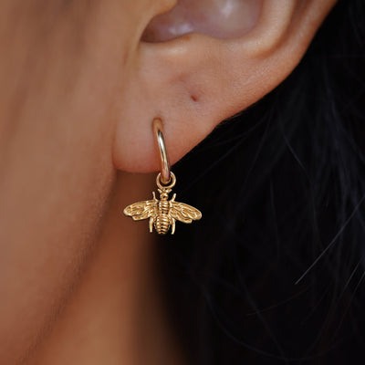 Close up view of a model's ear wearing a yellow gold Bee Charm on a Curvy Huggie Hoop