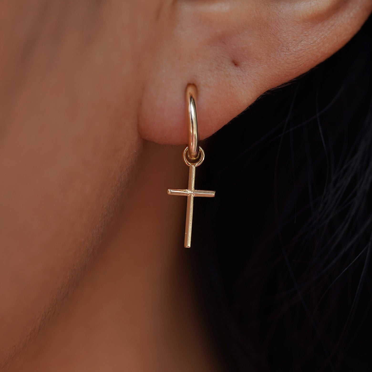 Close up view of a model's ear wearing a yellow gold Cross Charm on a Curvy Huggie Hoop