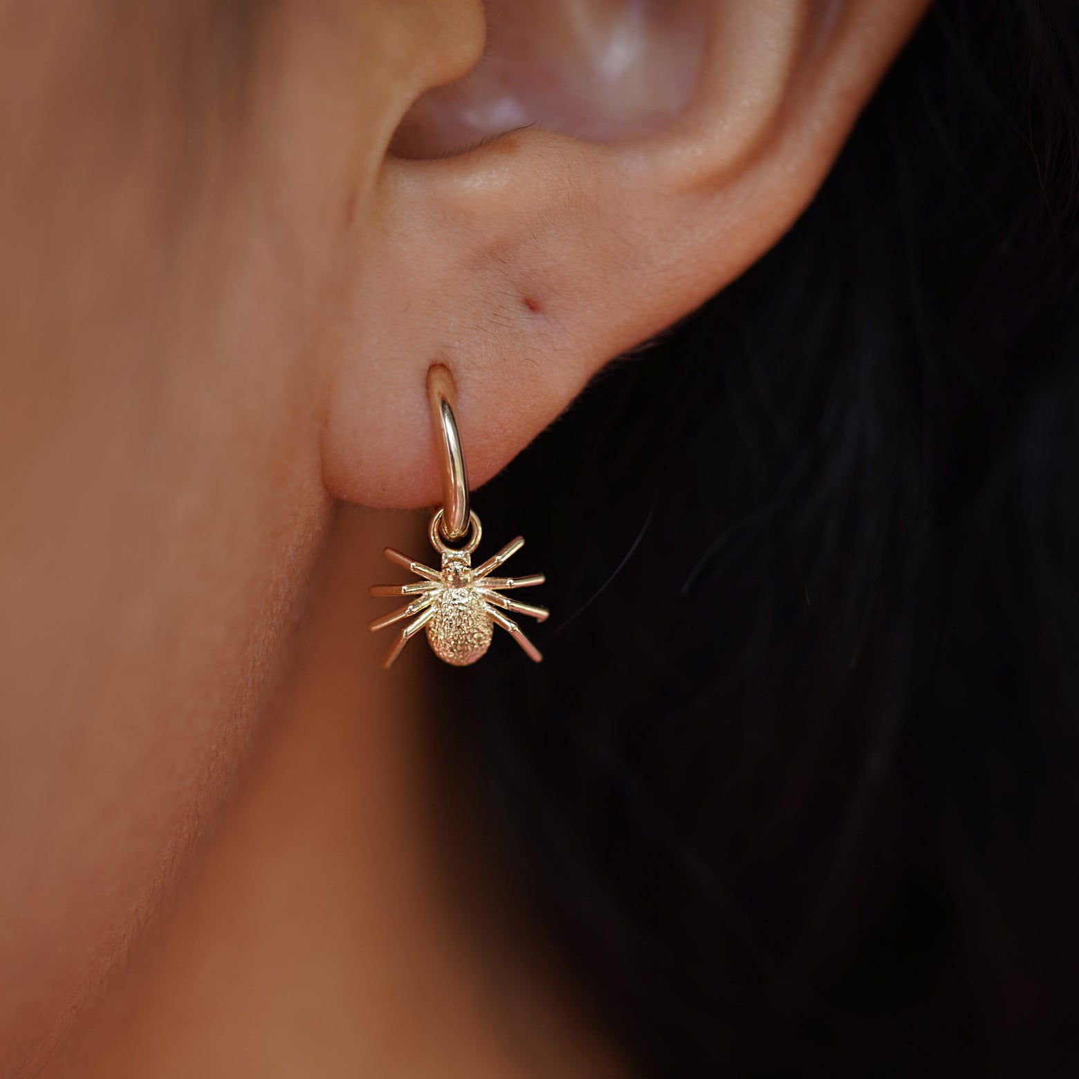 Close up view of a model's ear wearing a yellow gold Spider Charm on a Curvy Huggie Hoop