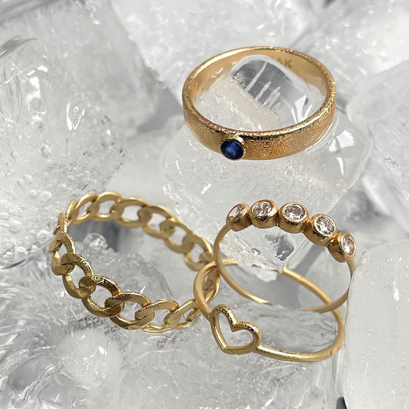 A 5 diamond ring, a sapphire industrial ring, a heart ring, and a curb ring sitting on ice cubes
