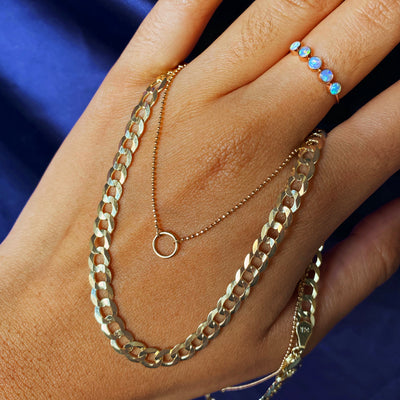 A model's hand holding Automic Gold necklaces in between their fingers while wearing a five opals ring