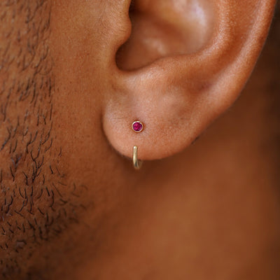 A model's ear wearing a 14 karat yellow gold ruby Gemstone Open Hoop