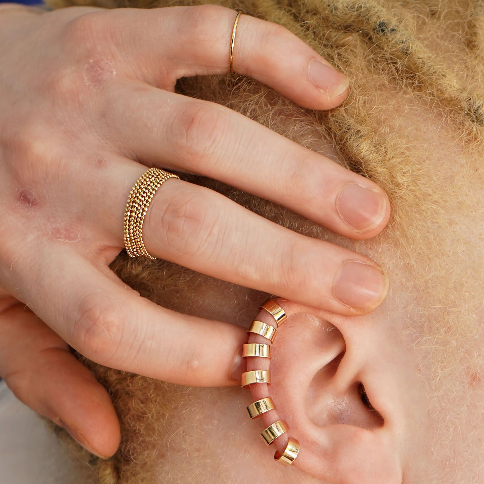 A model with their hand touching the top of their ear wearing many Thick Cuffs and a  stack of Bead Chain Rings
