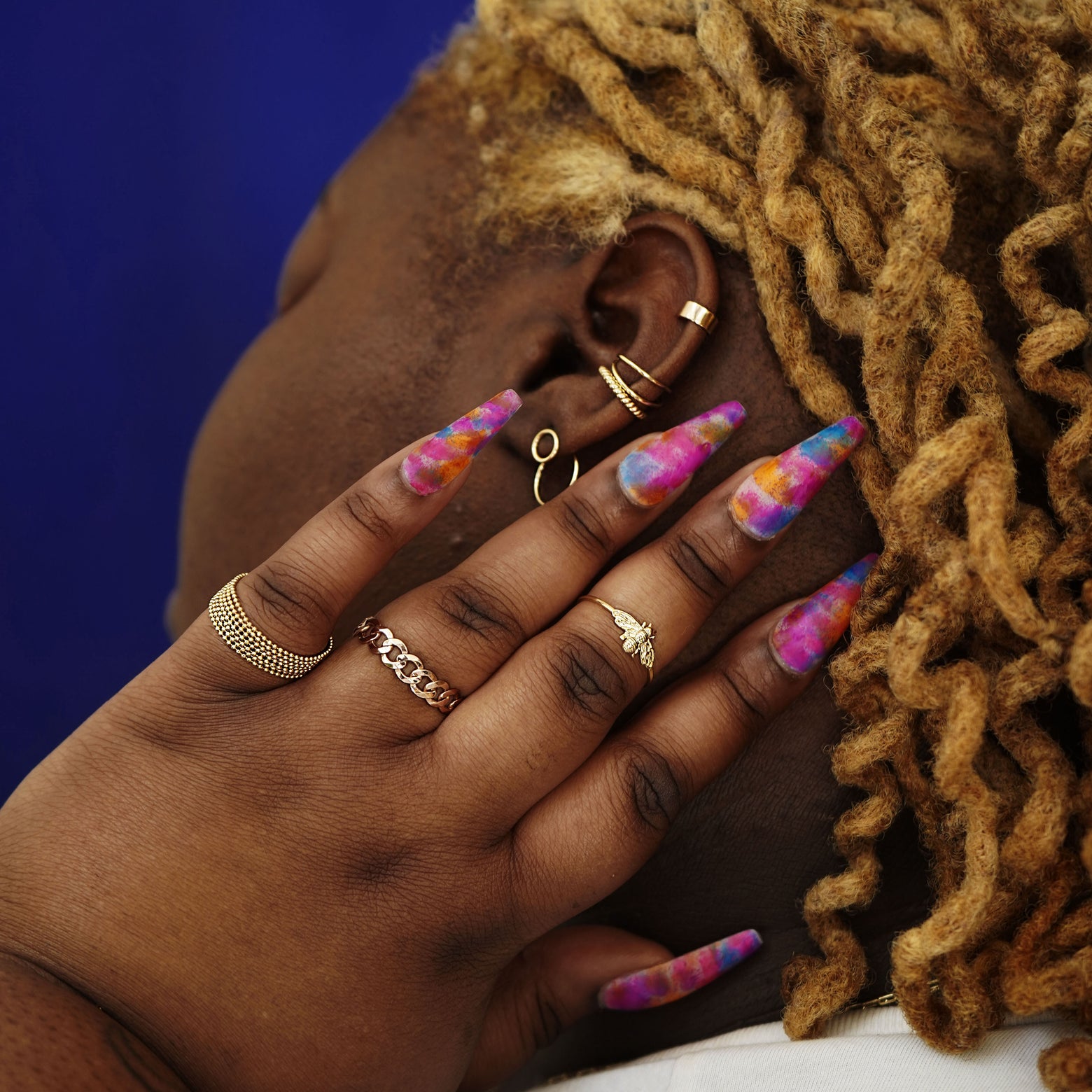 A model touching behind their ear wearing Automic Gold rings, earrings and ear cuffs