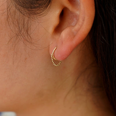 Close up view of a model's ear wearing a yellow gold Beaded Huggie Earring / Piercing