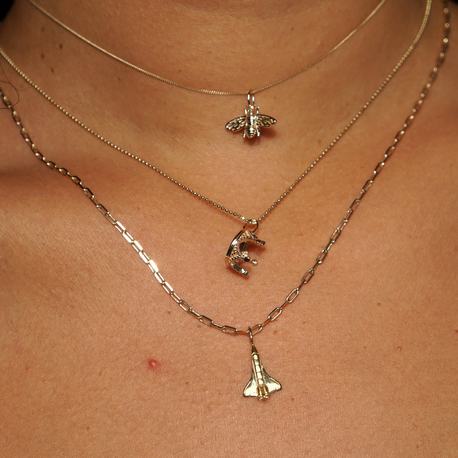 Model wearing a Bee Charm on an Essential Chain, A Crown Charm on a Bead Chain, and a Space Shuttle Charm on a Butch Chain