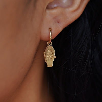 Close up view of a model's ear wearing a yellow gold Coffin Charm on a Curvy Huggie Hoop with the Coffin shown closed