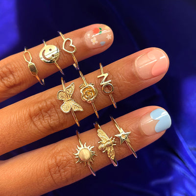Close up view of three fingers wearing a yellow gold sun ring and other Automic Gold rings