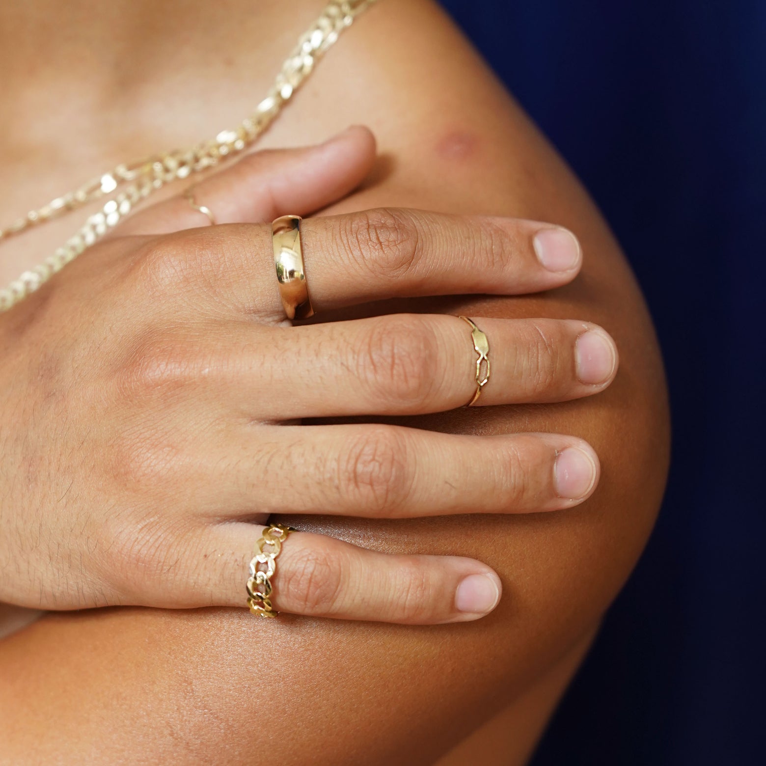 Close up view of a model's hand on their bare shoulder wearing various Automic Gold jewelry