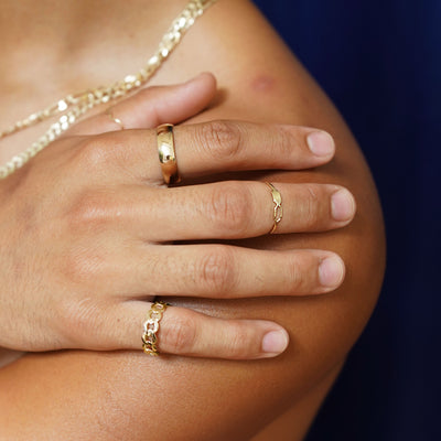 Close up view of a model's hand on their bare shoulder wearing various Automic Gold jewelry