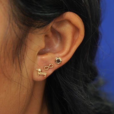 Close up view of a model's ear with an Infinity Earring, Dog Earring, and Coffee Cup Earring on different ear piercings