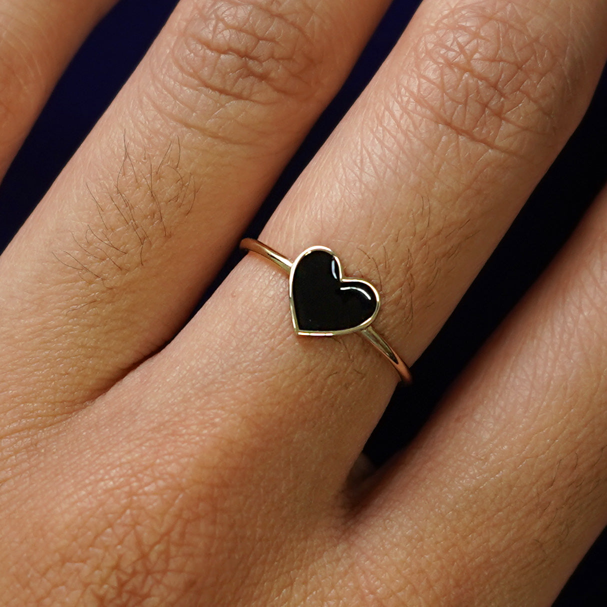 Close up view of a model's hand wearing a yellow gold black enamel heart ring