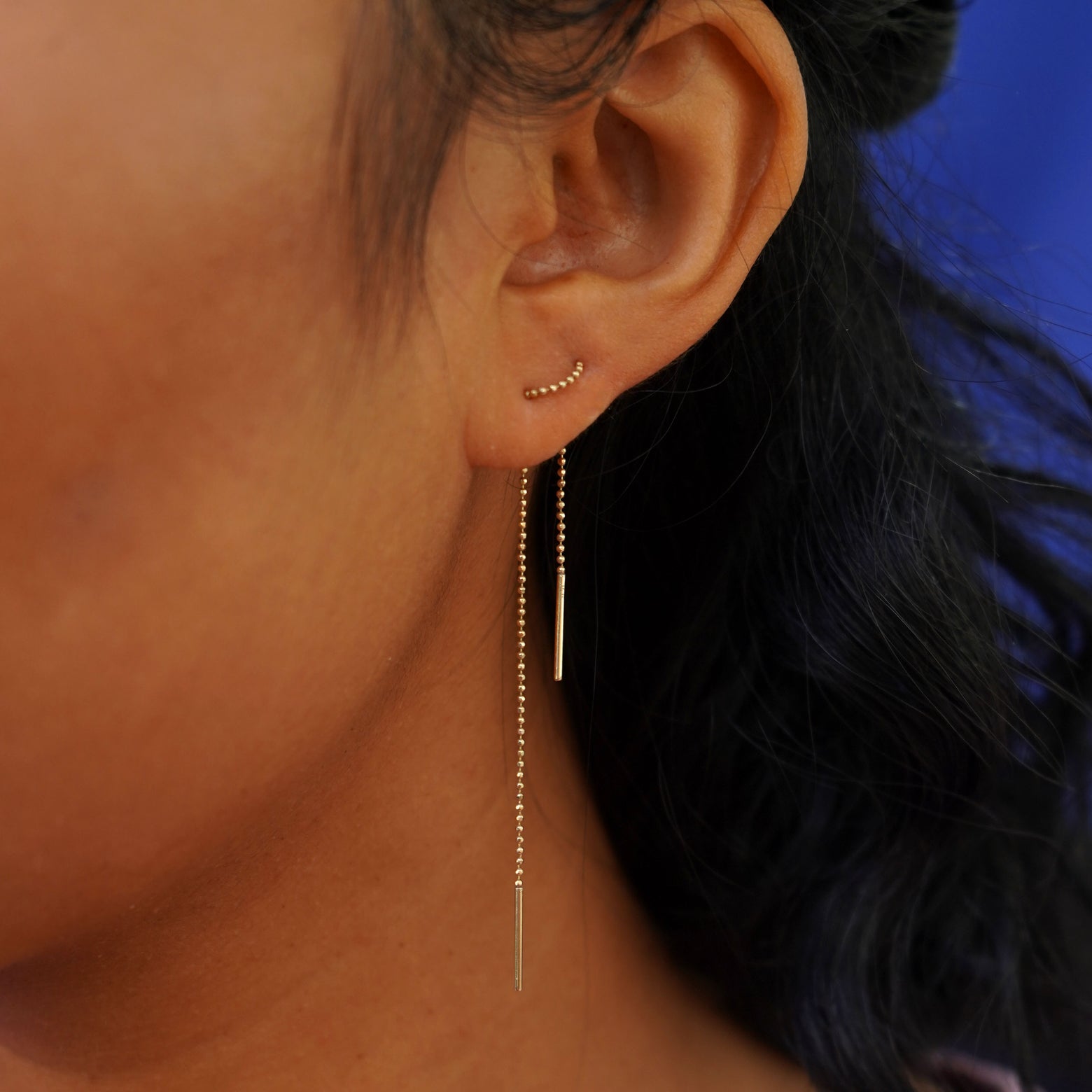 Close up view of a model's ear wearing a Threader through looped tightly in the front through two piercings and dangling