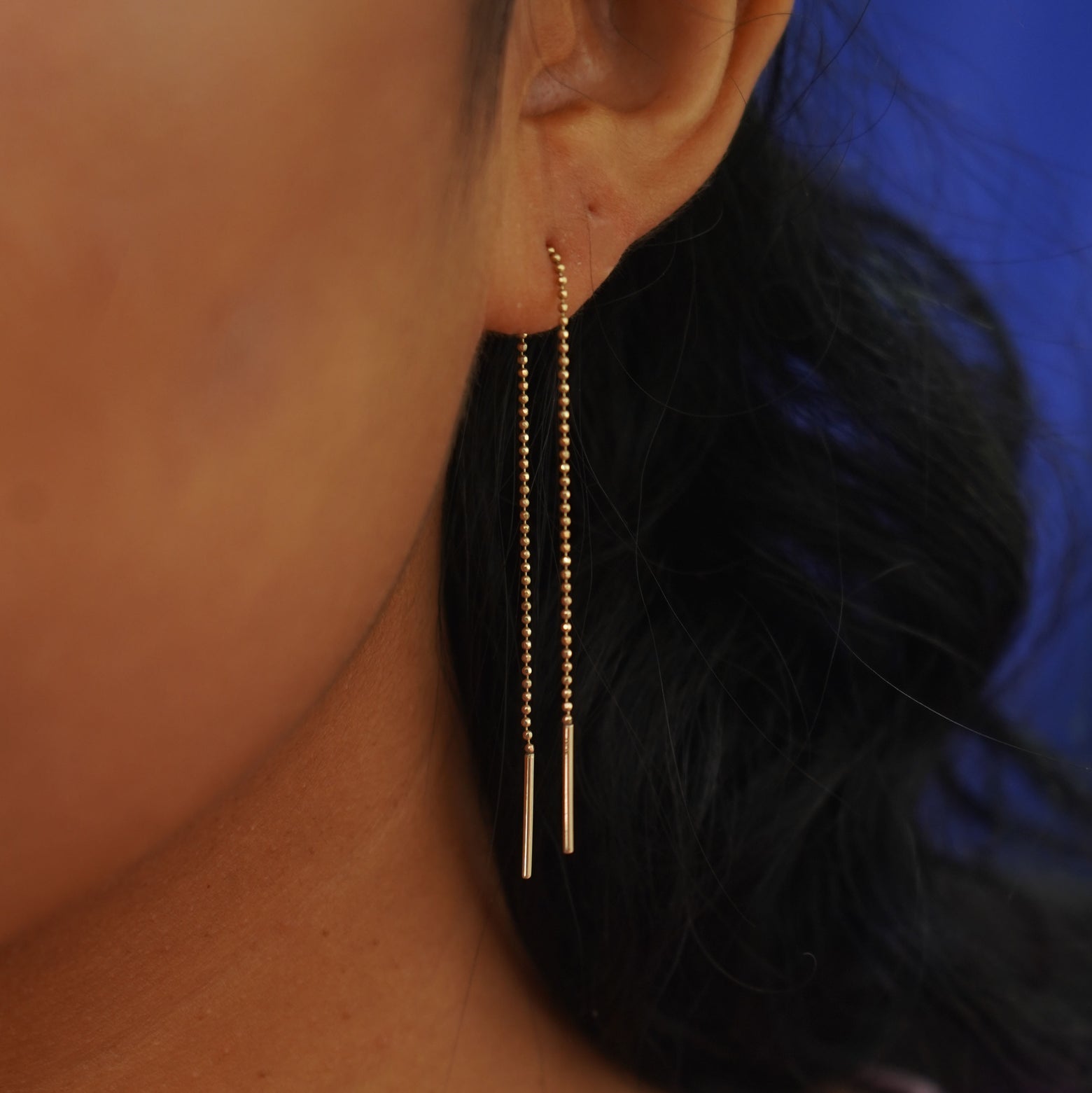 Close up view of a model's ear wearing with a yellow gold Threader dangling through a single lobe piercing