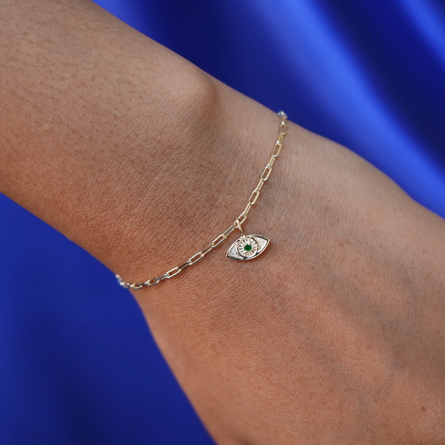 Close up view of a model's hand wearing an emerald Evil Eye Charm on a yellow gold Butch Bracelet