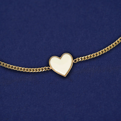 A solid 14k gold white enamel heart bracelet on a dark blue background