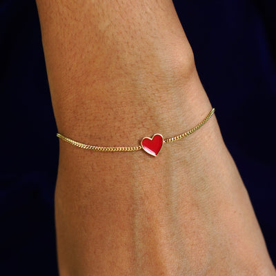 A model's wrist wearing a yellow gold red enamel heart bracelet