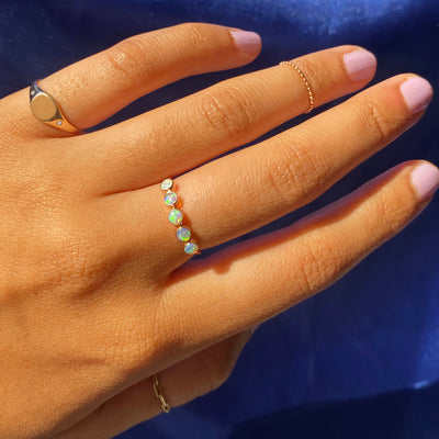 Close up view of a model's hand wearing a 5 opals ring, a diamond signet ring, a bead chain ring, and a butch ring