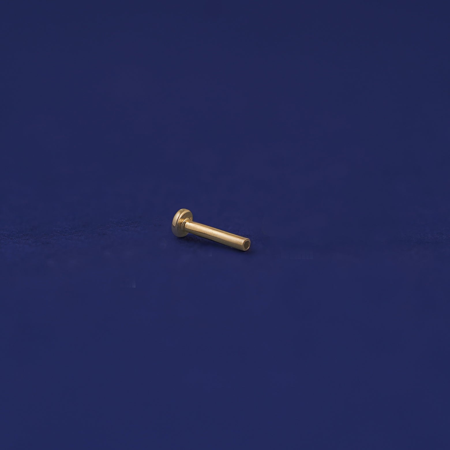 A 14k gold Flatback Piercing Backing on a dark blue background