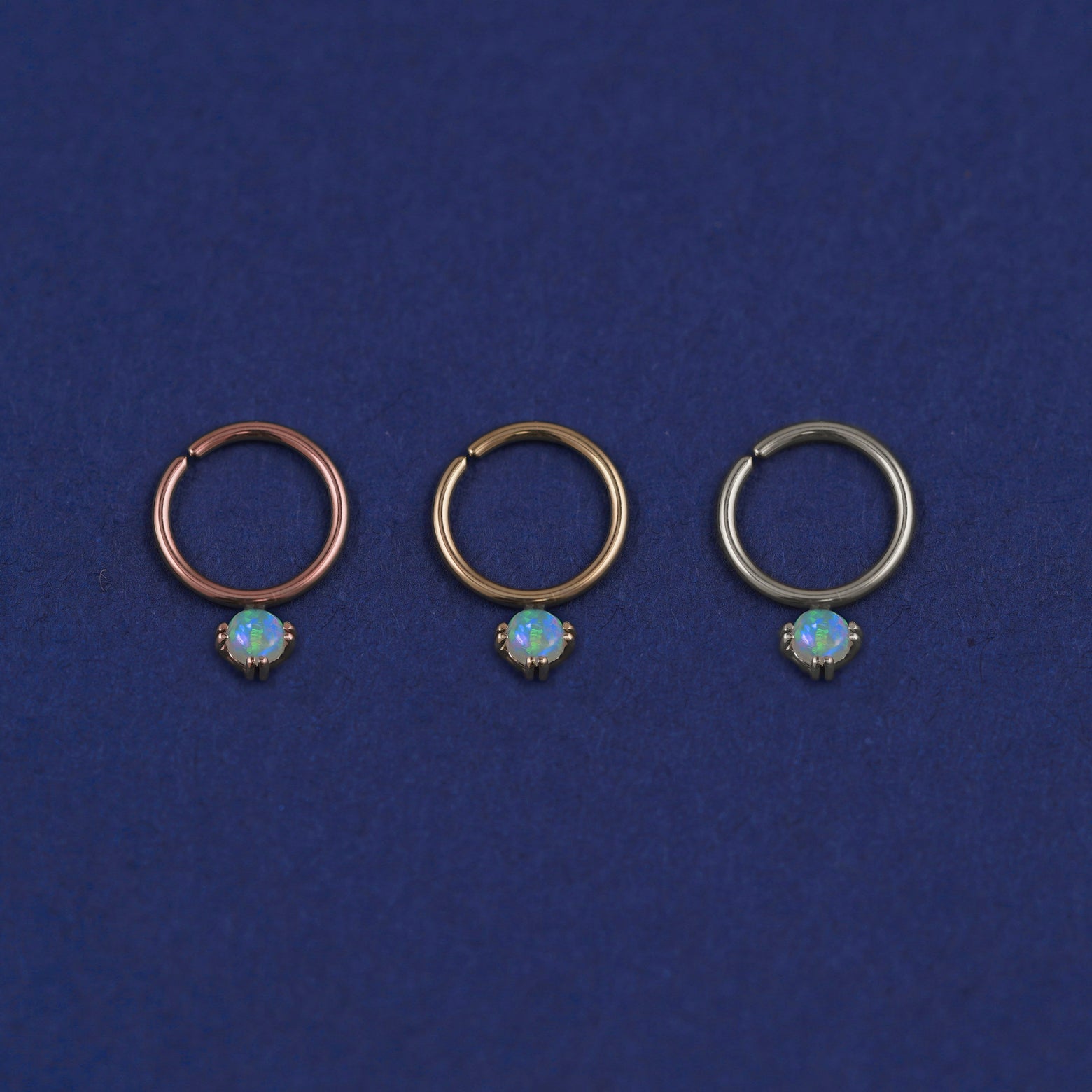 Three versions of the opal Pierced Gemstone Septum shown in options of rose, yellow, and white gold