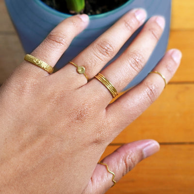 Close up view of a model's hand wearing a stack of yellow gold Hammered Rings along with other Automic Gold rings