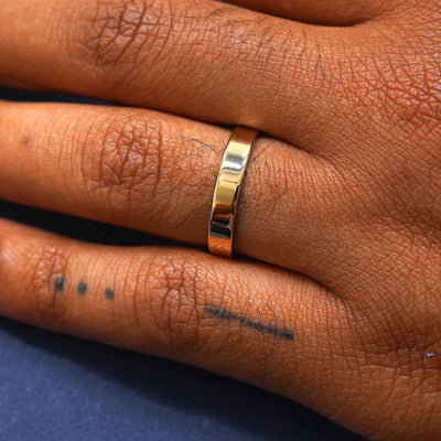 Close up view of a model's hand wearing a 14 karat yellow gold Industrial Mirror Band on their ring finger