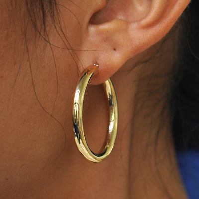 Close up view of a model's ear wearing a yellow gold Large Tube Hoop Earring