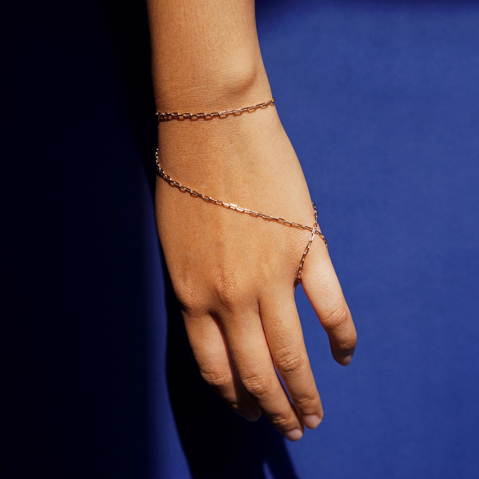 Close up view of a model wearing a 14k rose gold Wrap Necklace as a hand chain that wraps around their pinky finger